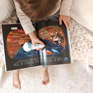 A boy reading the Discover Talking Book by pointing the talking pen to an illustration listening to the dolphin sound effect while learning S.T.E.M. facts screen free. 